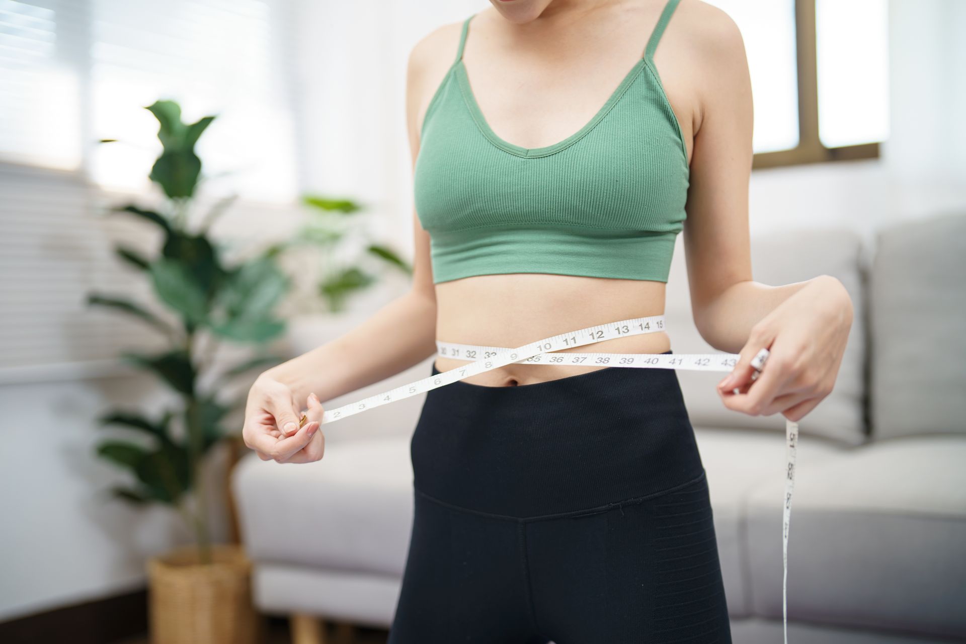 A woman is measuring her waist with a tape measure.