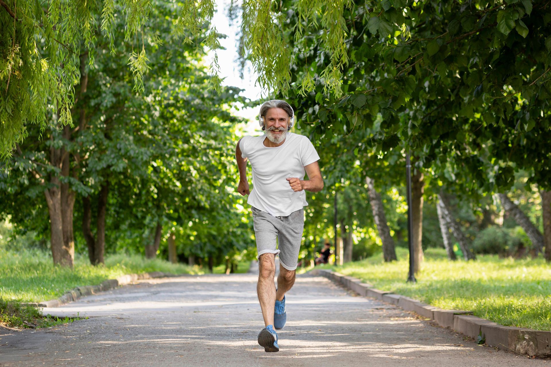 An elderly man is running on a path in a park.