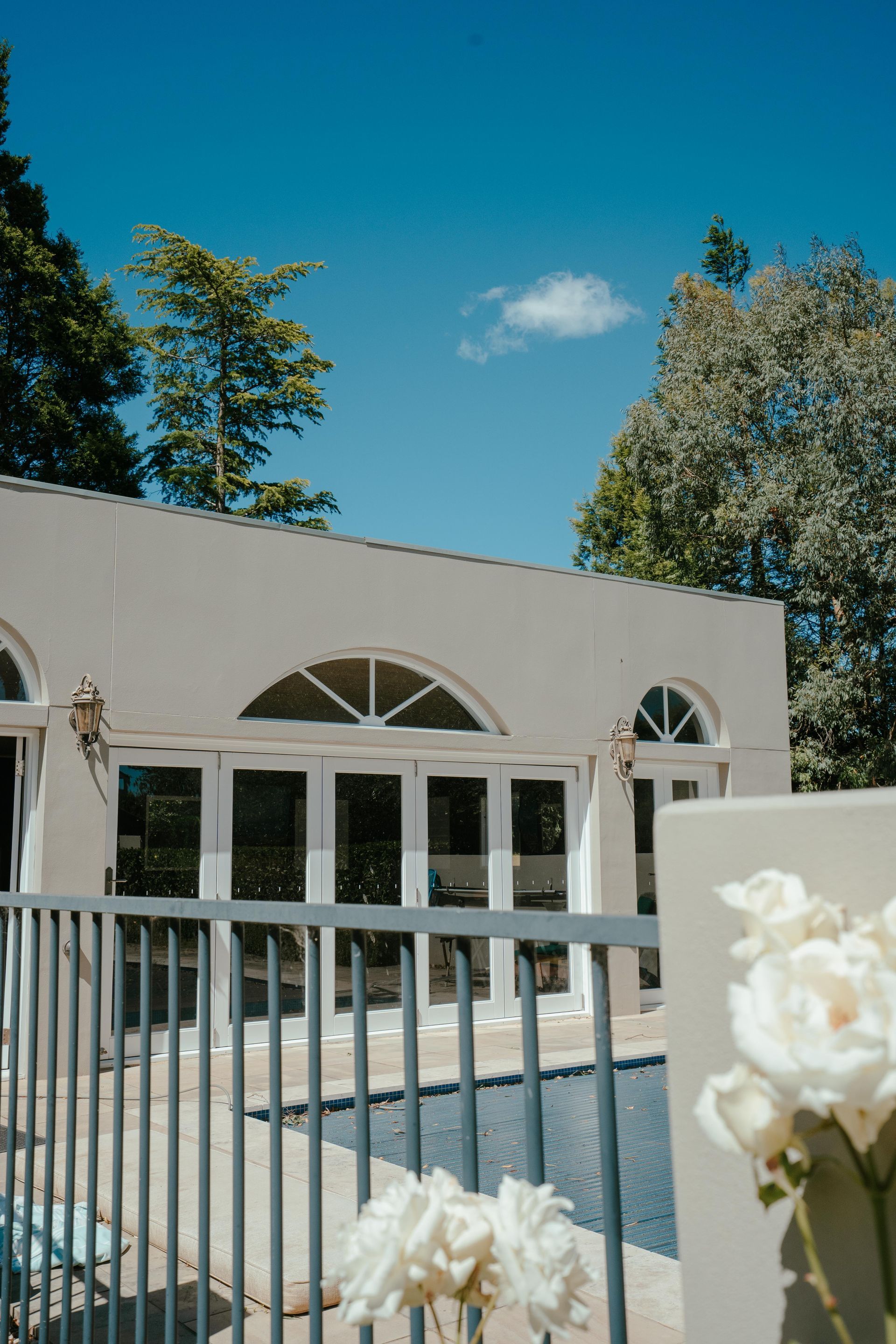 Beige building with arched windows, pool, white roses, and blue sky. — Mittagong Painting in Welby, NSW