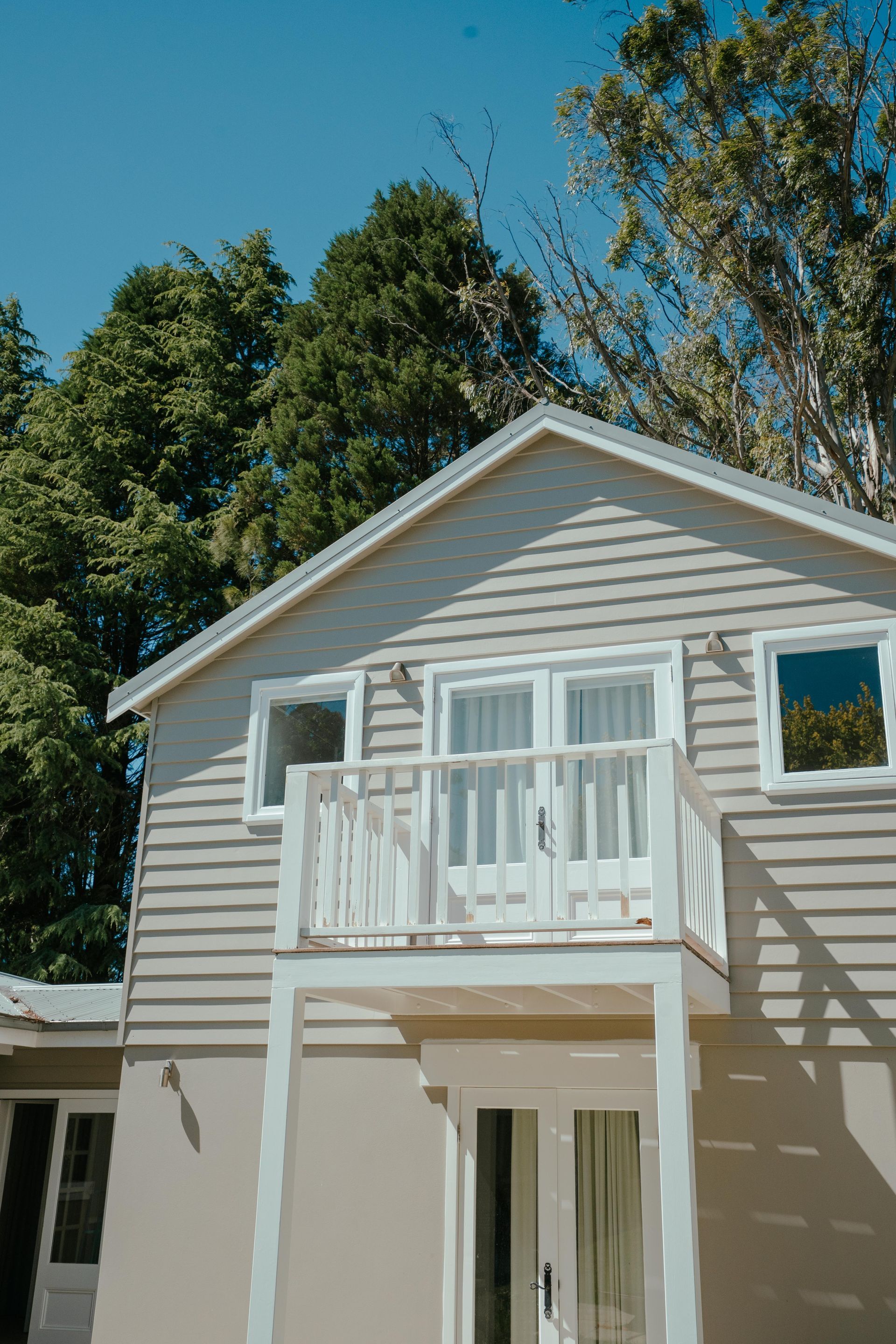 Two-story light gray house with balcony and white railing, with green trees and blue sky background. — Mittagong Painting in Welby, NSW