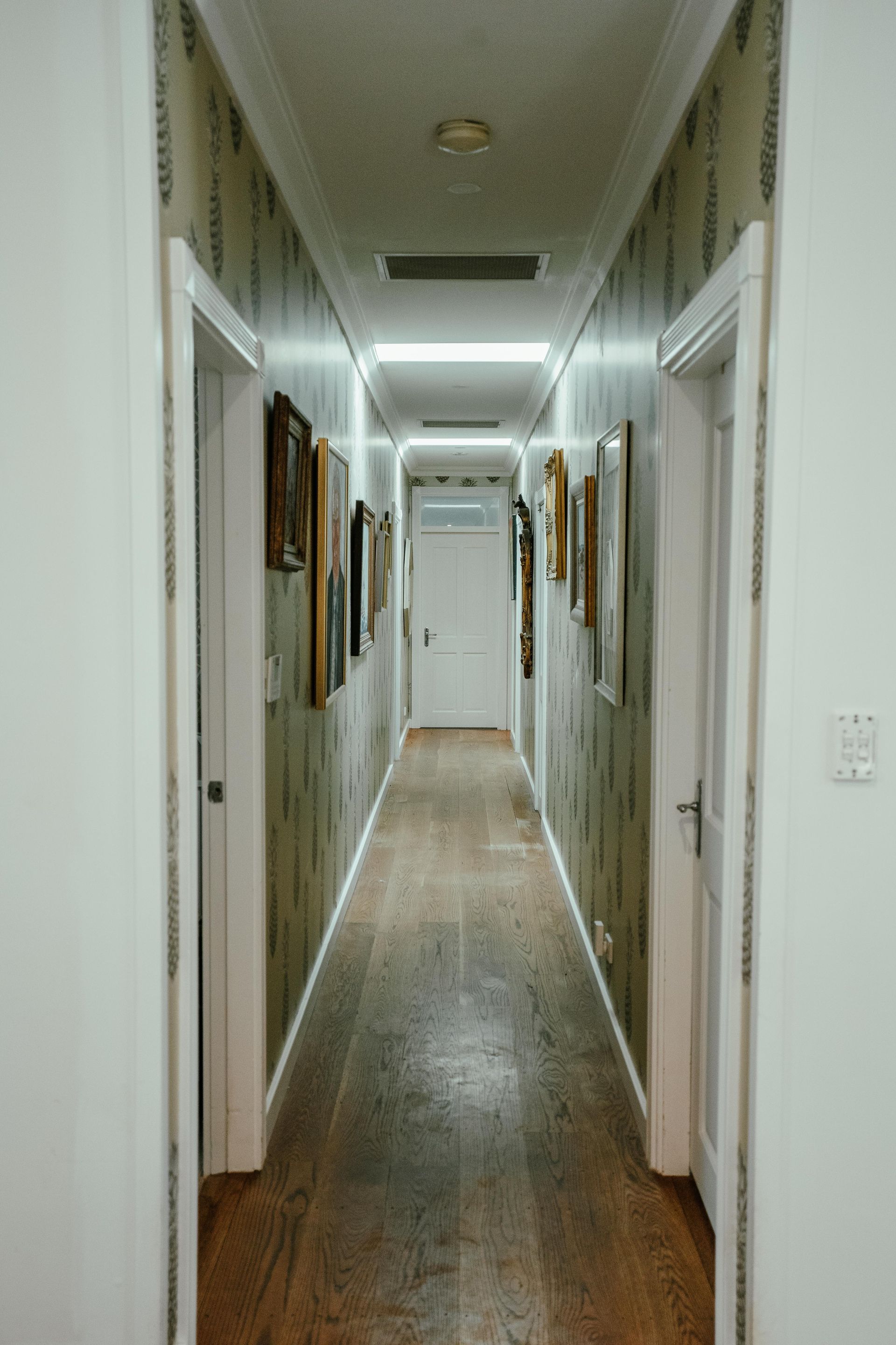 Long hallway with wood flooring, doors, and artwork on patterned wallpapered walls. — Mittagong Painting in Welby, NSW