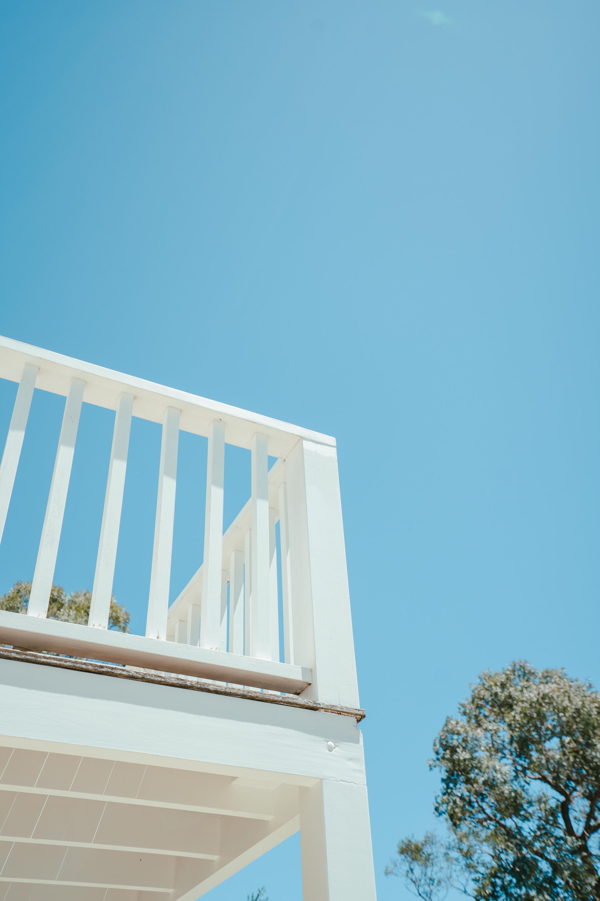White balcony railing against a bright blue sky, with a tree in the corner. — Mittagong Painting in Moss Vale, NSW