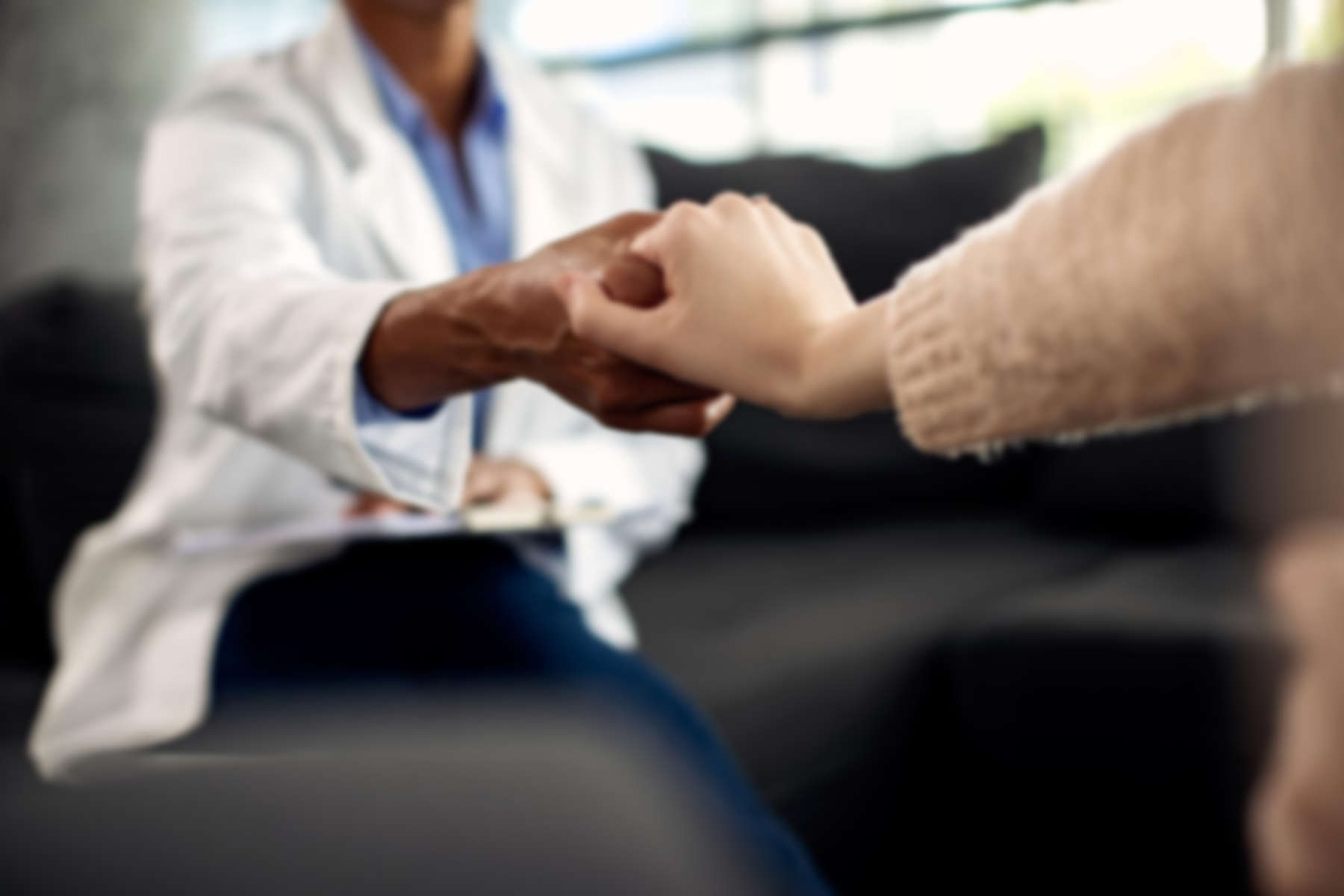 A doctor is holding a patient 's hand while sitting on a couch.