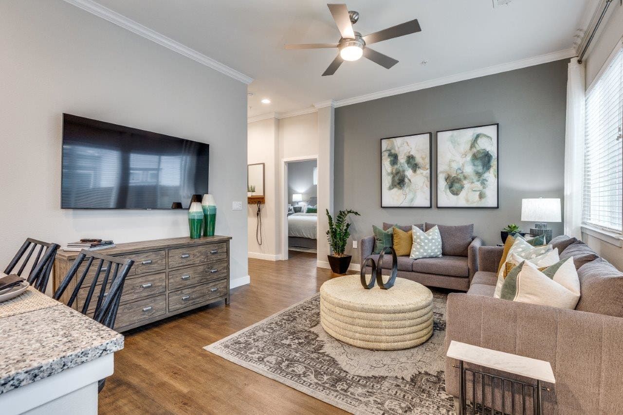 A living room with a couch, ottoman, television, and ceiling fan.