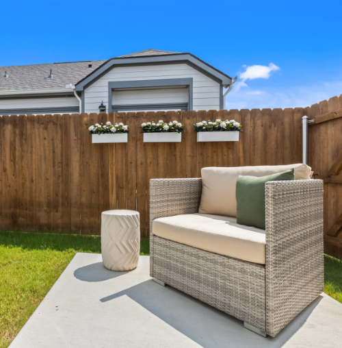 A wicker couch sits in front of a wooden fence.