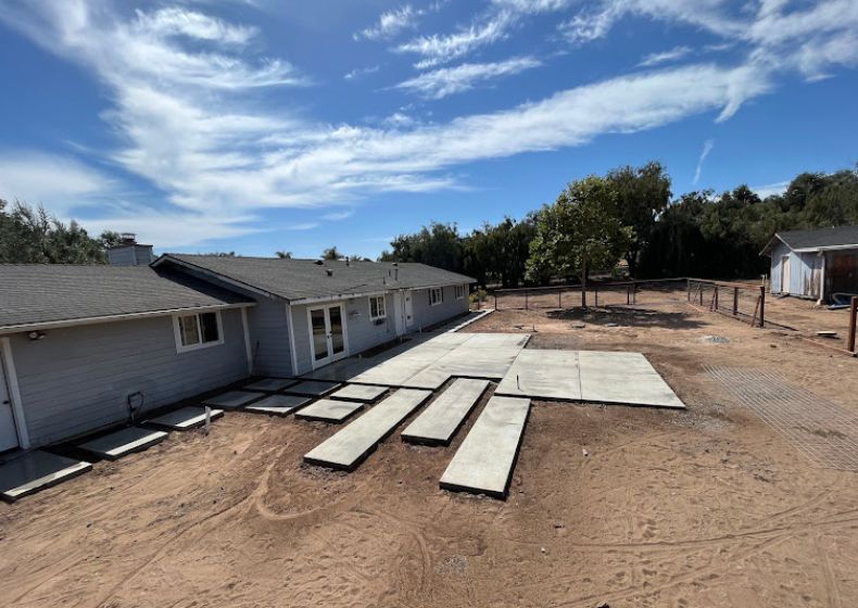 Residential building with large concrete panels laid out in a dirt yard under a blue sky
