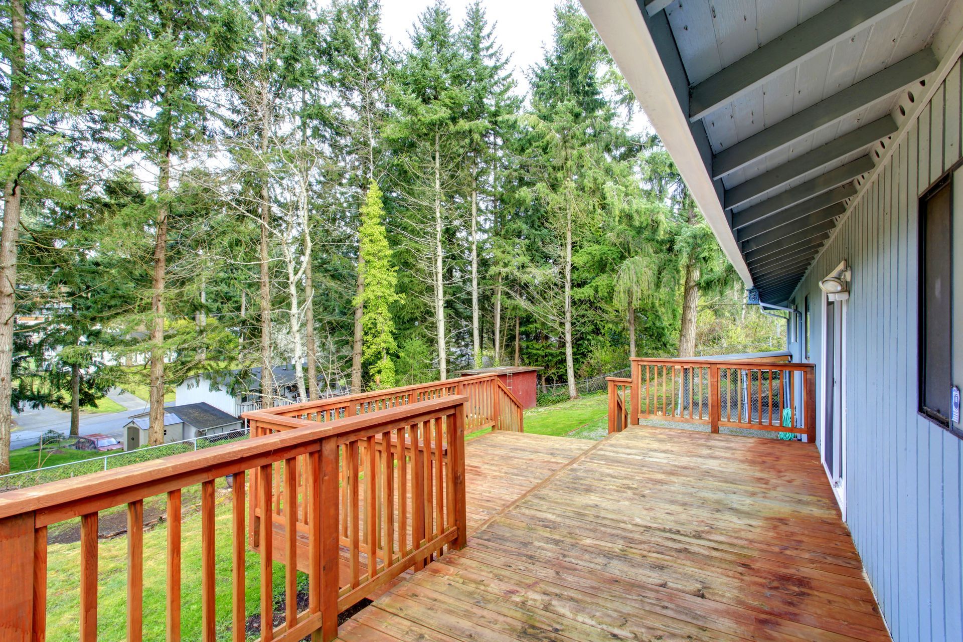 Wooden deck beside a house, overlooking a wooded yard with tall trees and greenery.