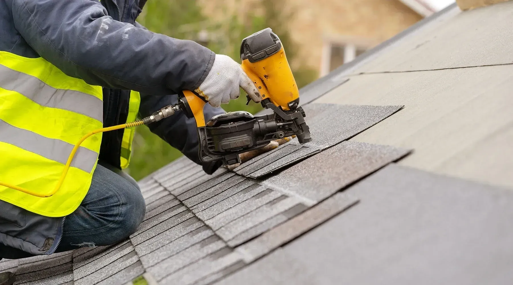 Worker cutting roofing shingles with a yellow power saw on a sloped roof