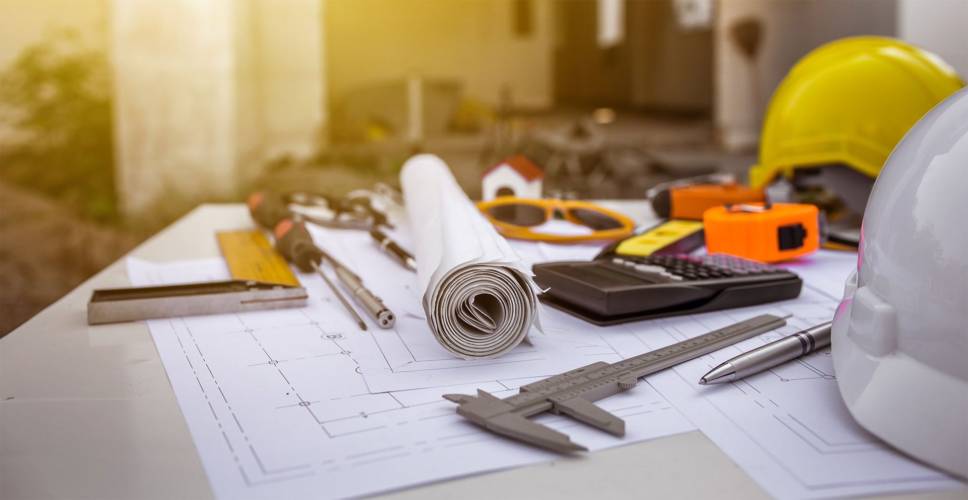 Architectural plans with rolled blueprints, ruler, pencil, hardhat, and house model on a desk