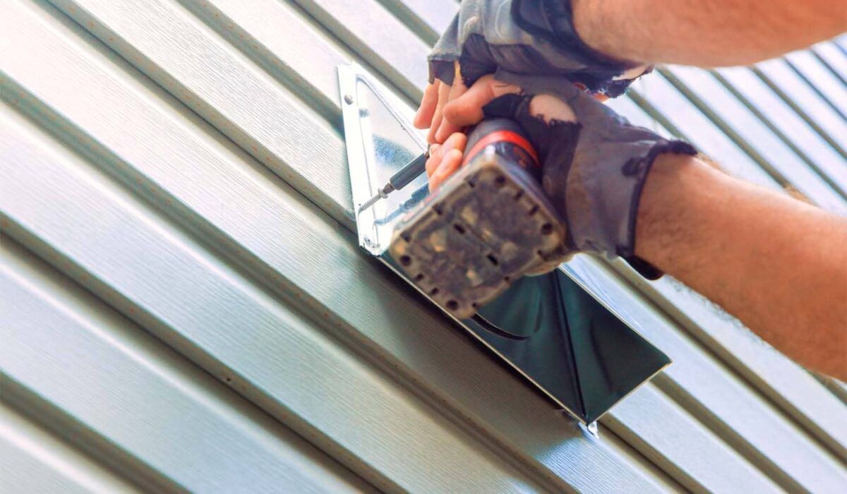 Hands using a power drill to fasten metal roofing panels under bright light