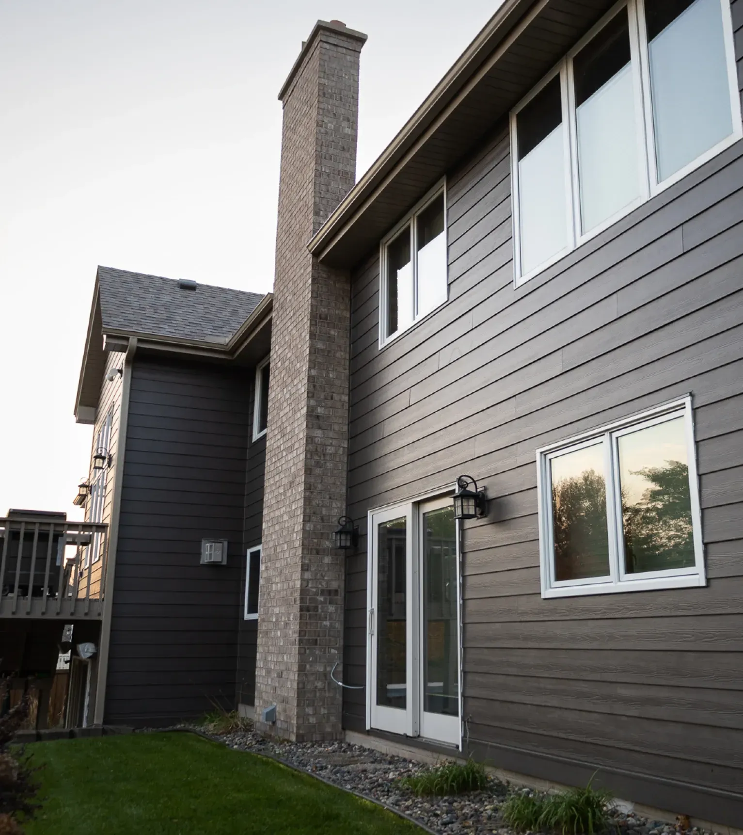 Two-story brown house exterior with chimney, sliding glass door, and windows, viewed from the backyard