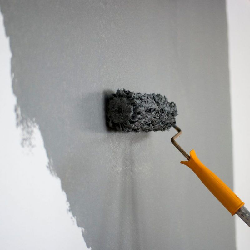Paint roller applying gray paint to a white wall, creating a smooth painted section.