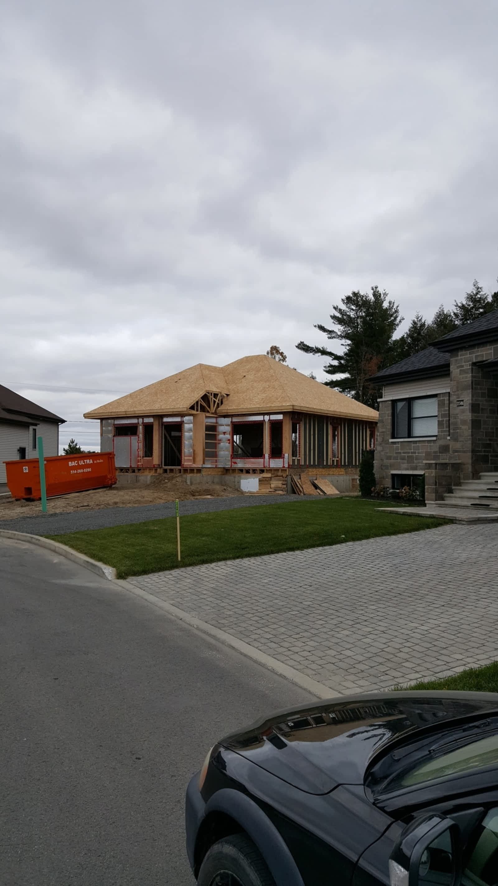 A car is parked in front of a house under construction.