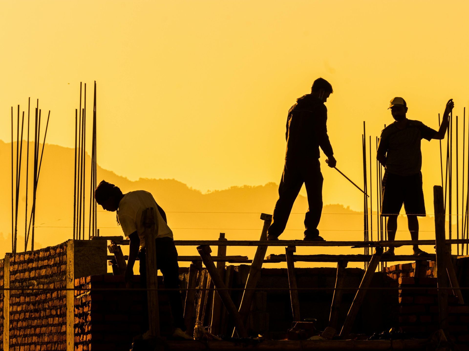 A group of construction workers are working on a building at sunset.