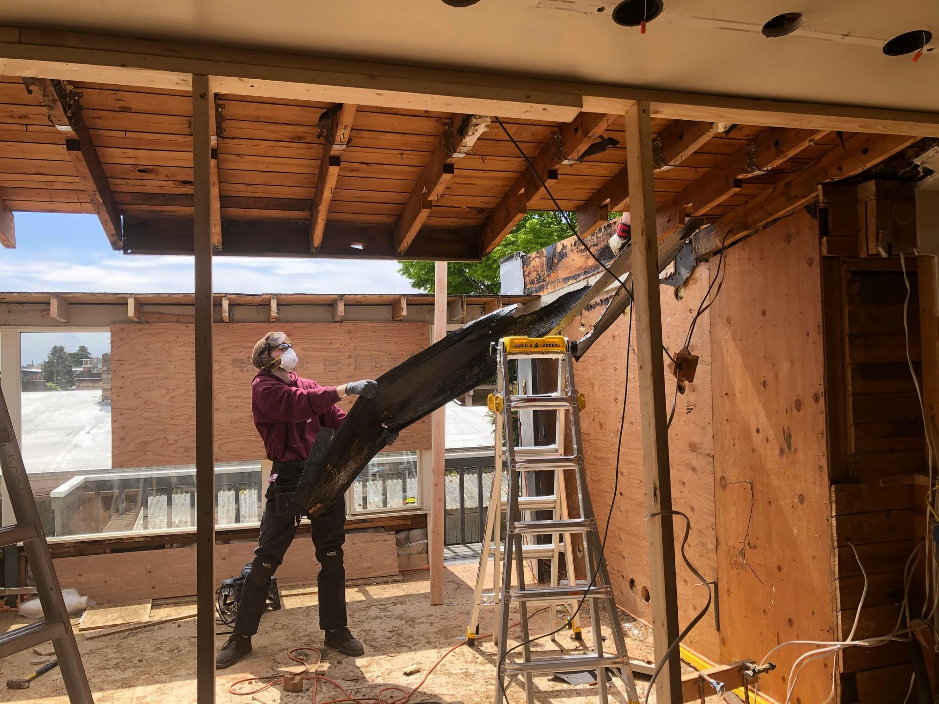 A man wearing a mask is standing next to a ladder in a room under construction.