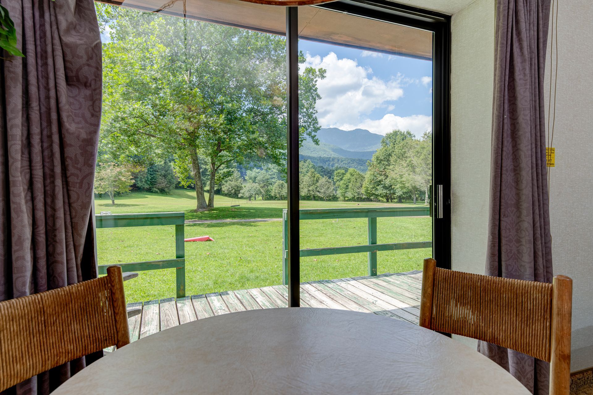 A dining room with a table and chairs and a view of a field through a sliding glass door.