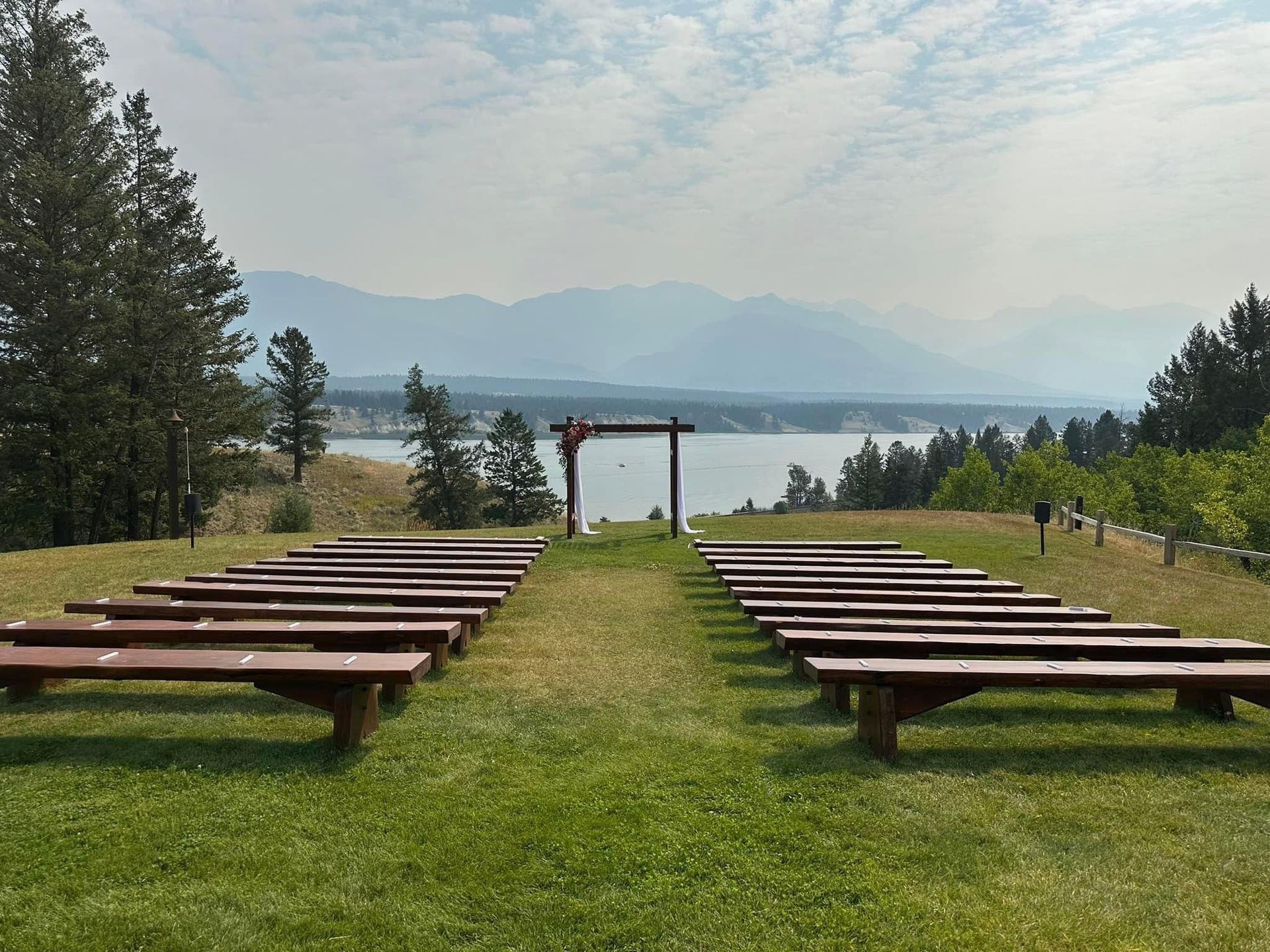 A row of wooden benches in a grassy field with mountains in the background.