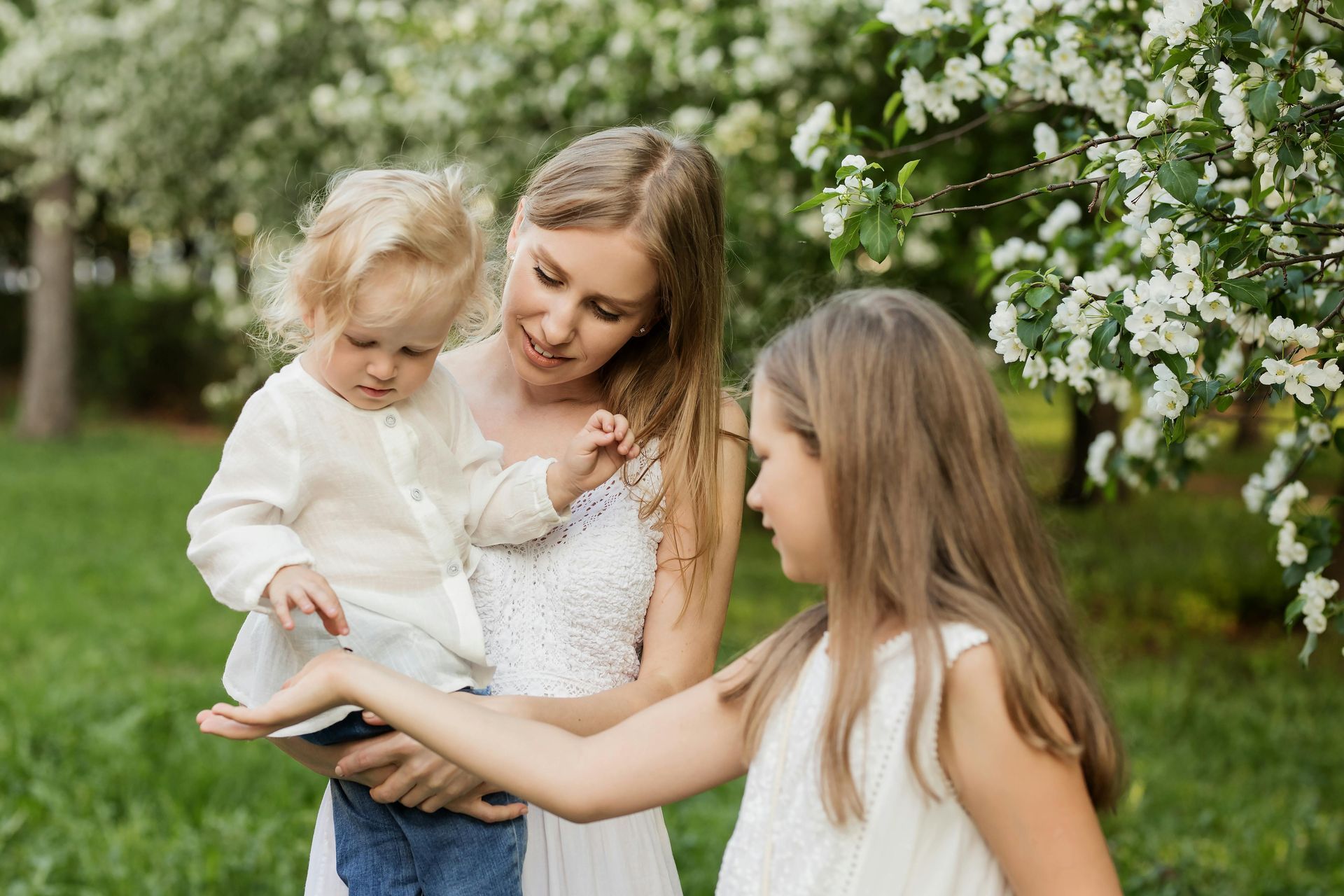 A woman is holding two children in her arms in a park.