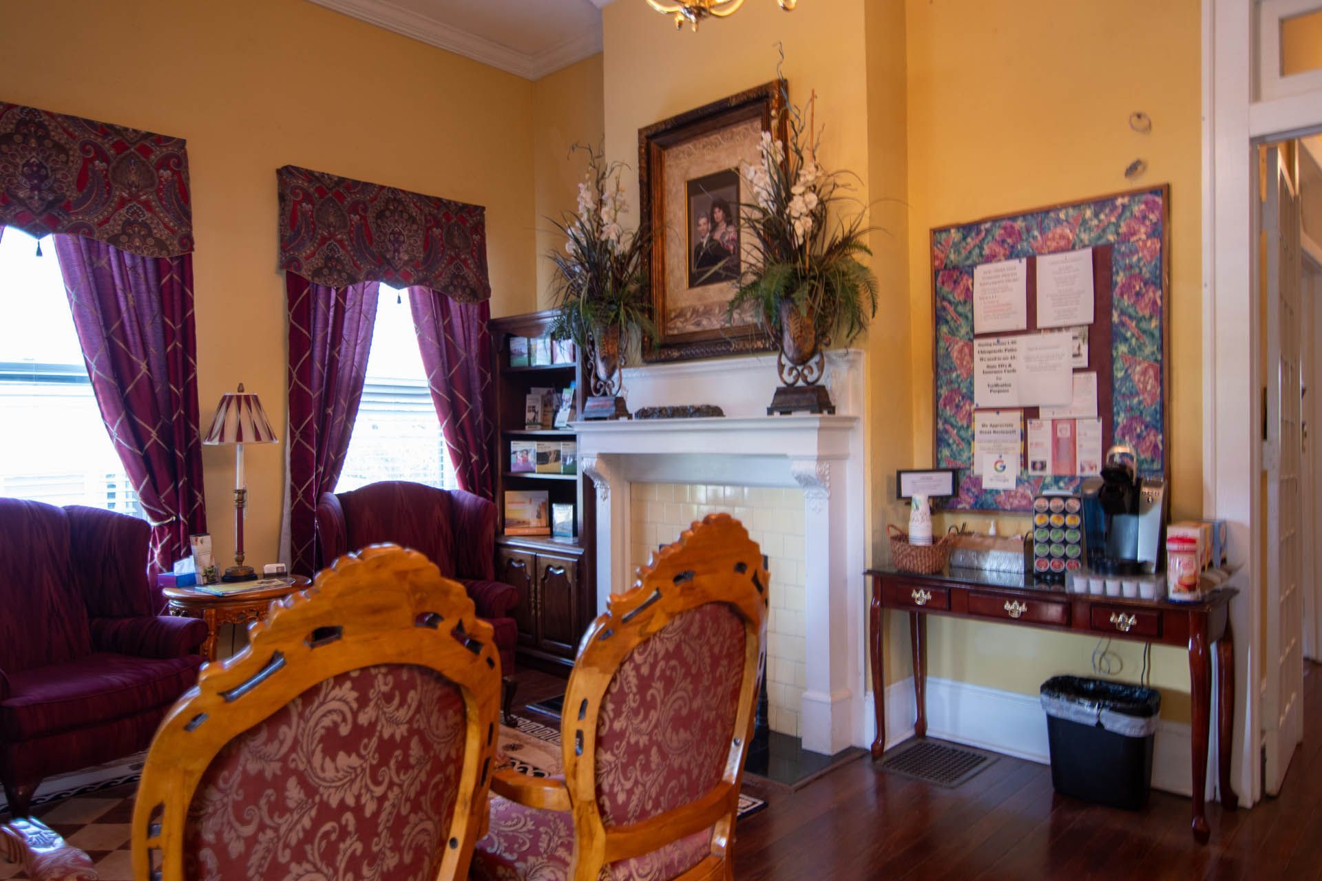 A living room with a fireplace , chairs , a desk and a bulletin board.