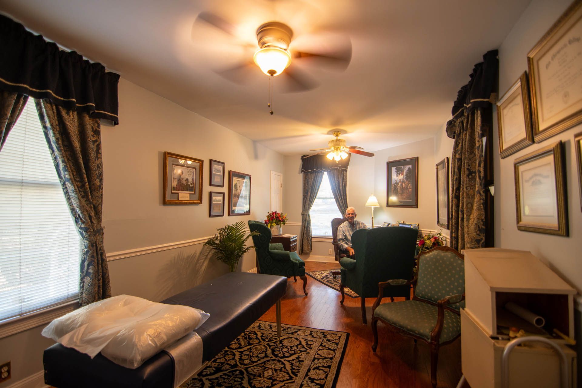A man is sitting in a chair in a living room with a ceiling fan.
