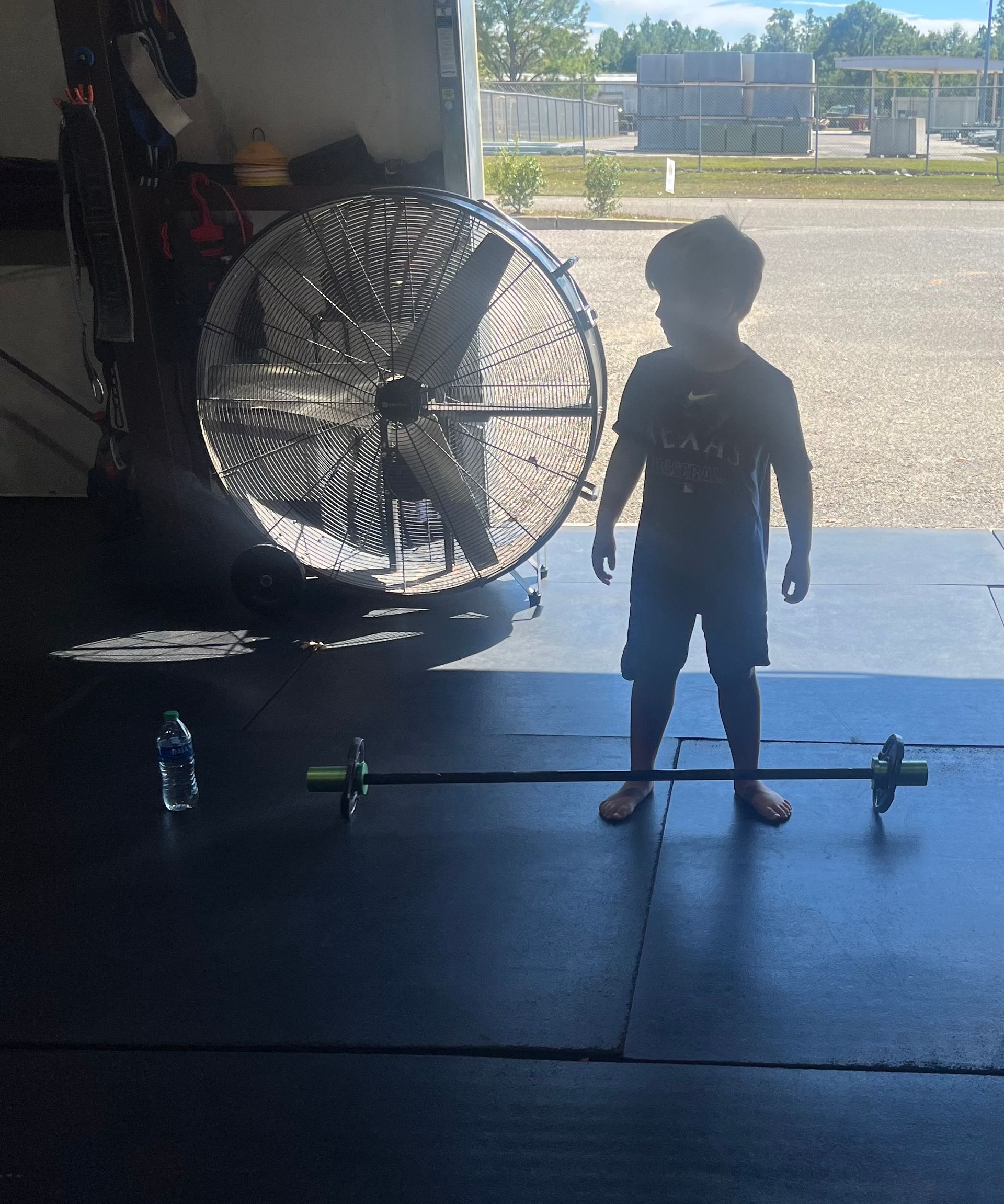 A young boy stands in front of a fan in a garage