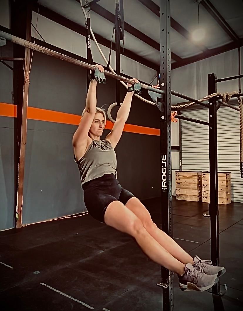A woman is doing a pull up on a bar in a gym.