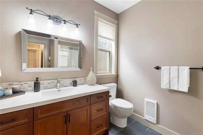 Bathroom with wooden vanity, white countertop, large mirror, toilet, and tan walls.