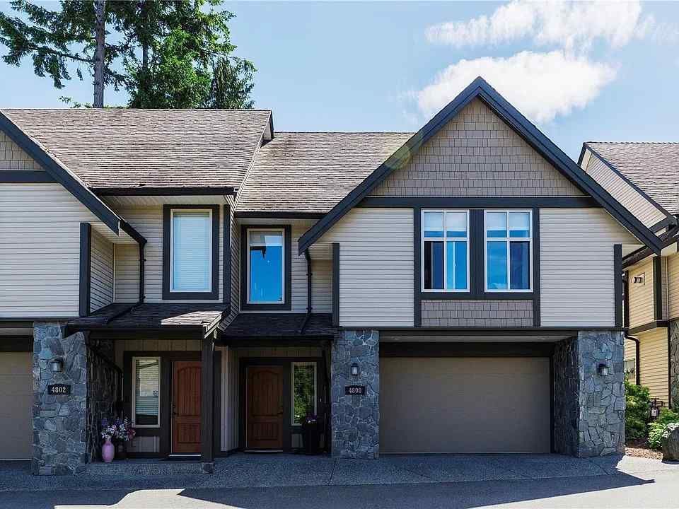 Townhouse exterior with beige siding, brown roof, stone pillars, and garage door, set against a blue sky.