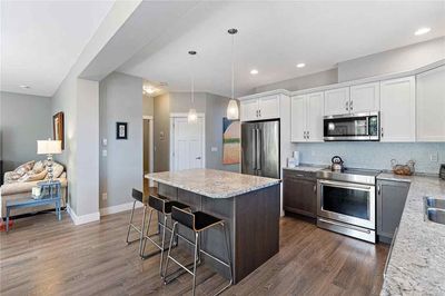 Modern kitchen with island and seating, stainless steel appliances, and hardwood floors.