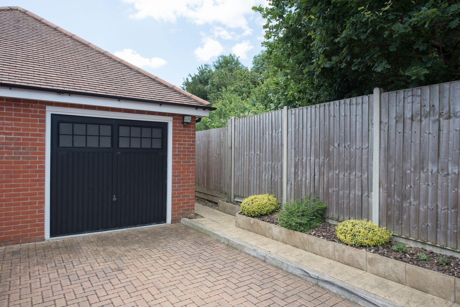 A brick garage with a black garage door next to a wooden fence.