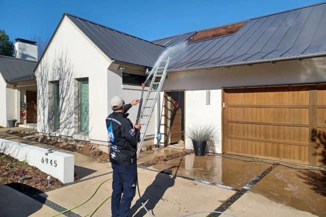 A man is cleaning the roof of a house with a pressure washer.