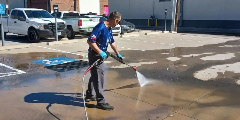 A man is using a high pressure washer to clean a parking lot.