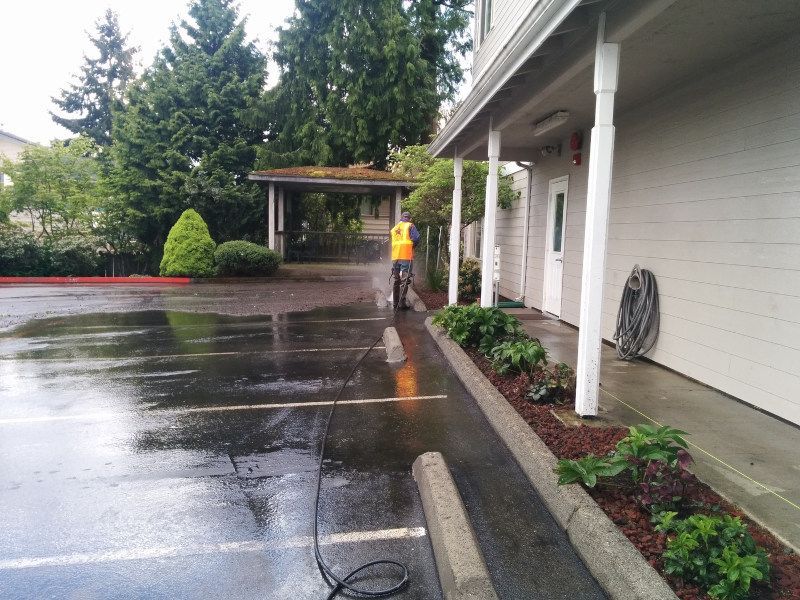 A man in an orange vest is cleaning a parking lot