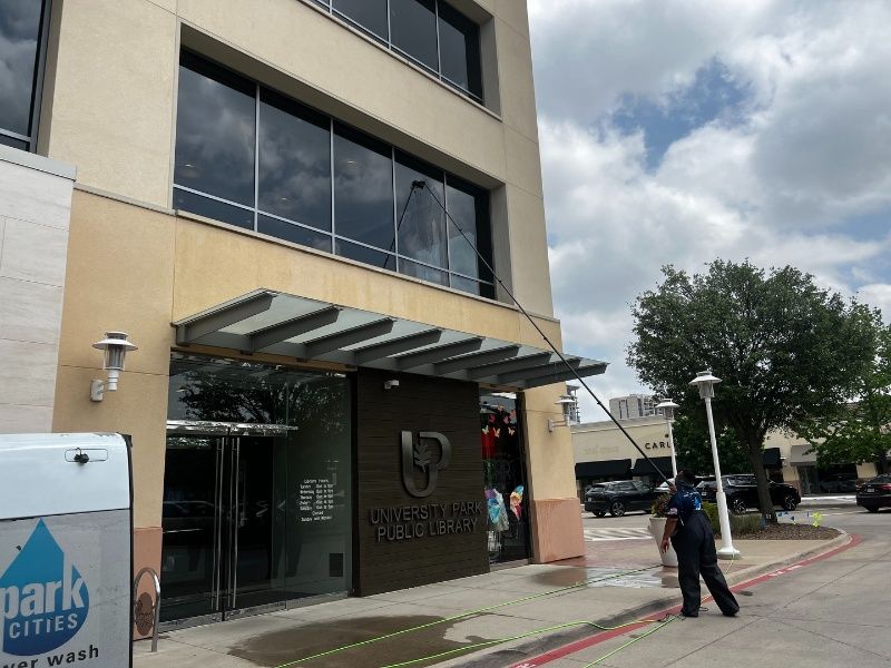A man is cleaning the windows of a building that says park cities