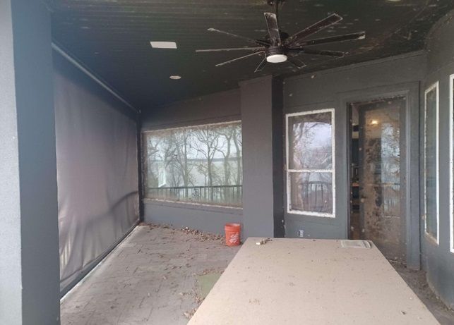 A screened in porch with a ceiling fan and a table.
