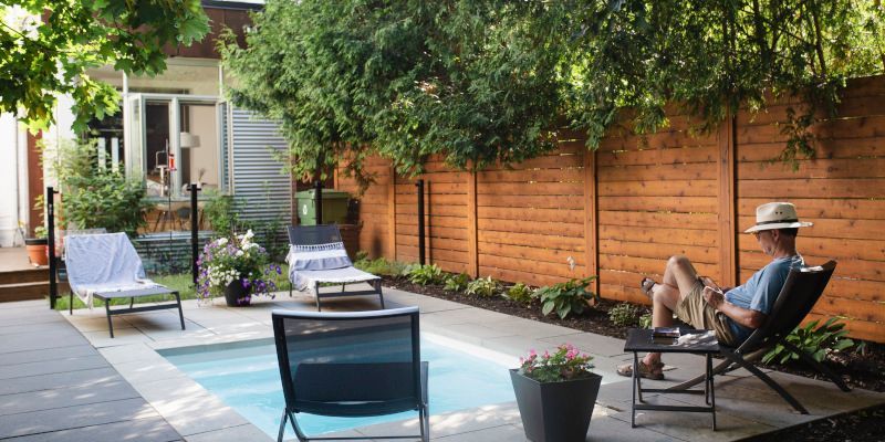 A man is sitting in a chair in a backyard next to a pool.