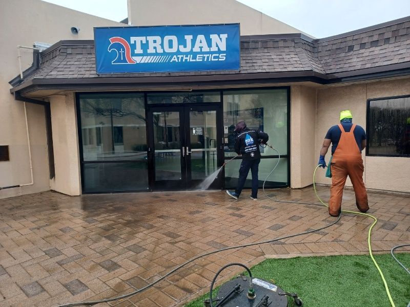 A man is cleaning the outside of a building with a sign that says trojan athletics.