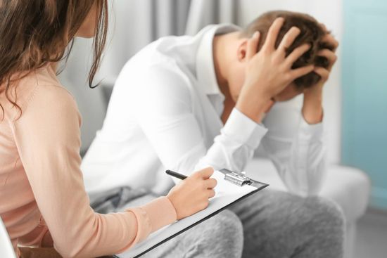 Man with head in hands next to lady with clipboard
