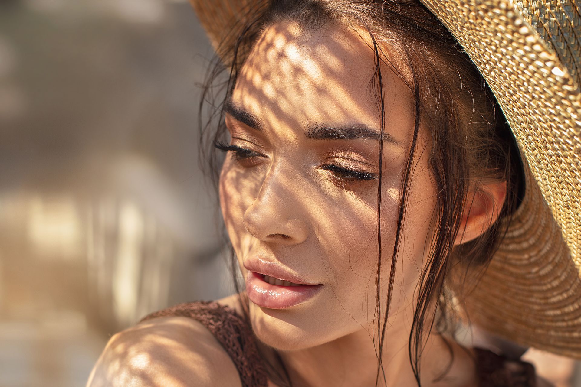 A close up of a woman wearing a straw hat to help block bright sunlight from her face,