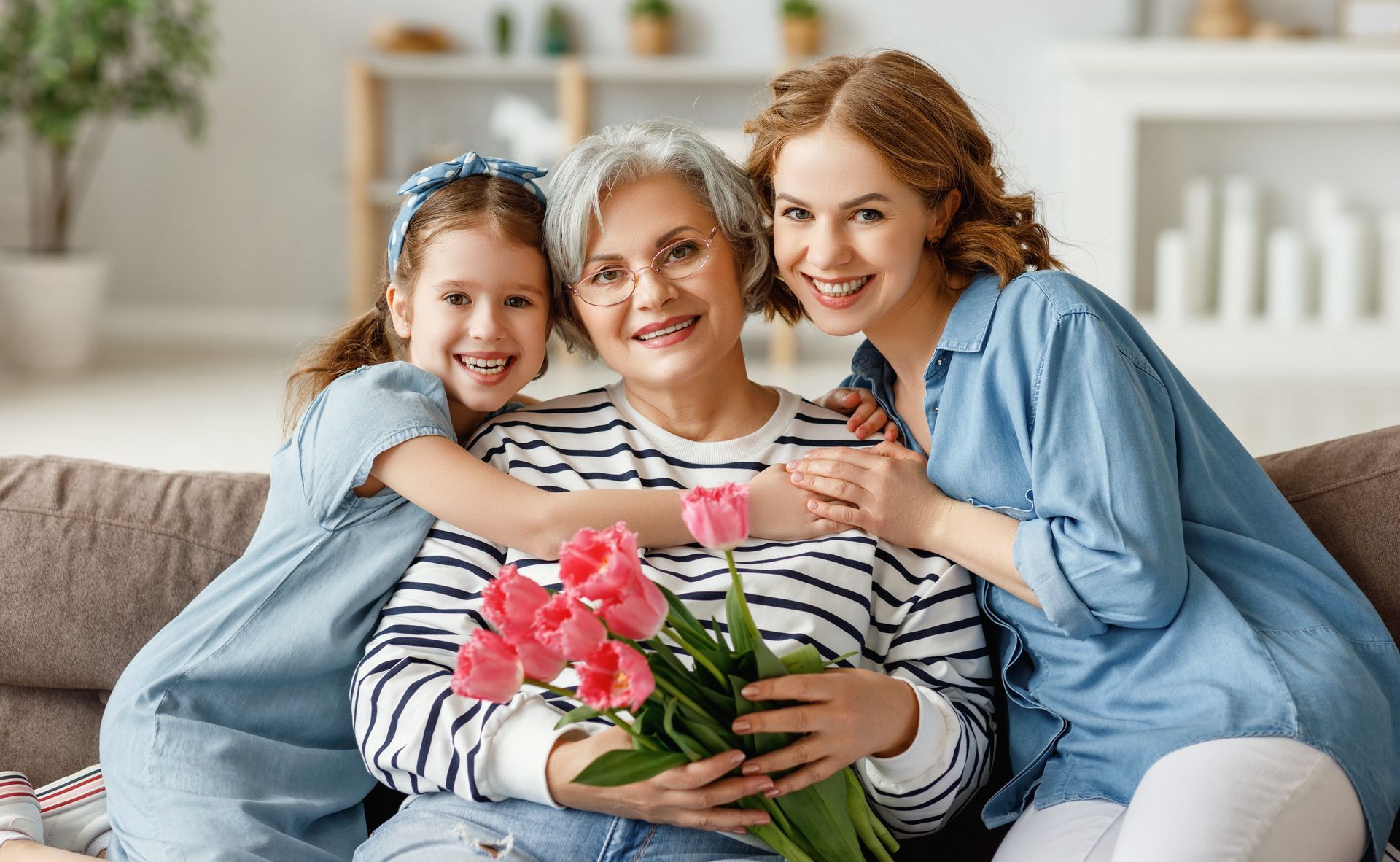 Woman sitting on sofa with her older mom and daughter smiling on mother's day