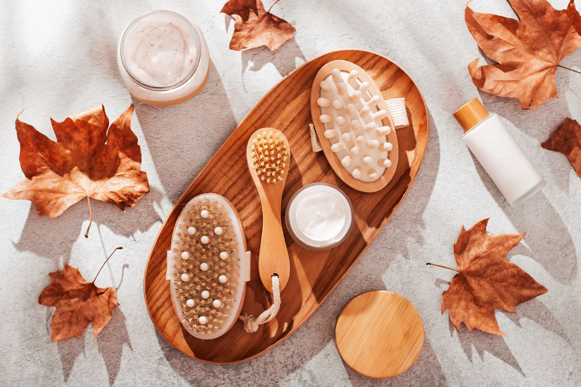 A wooden tray filled with brushes , skincare cream , and Fall leaves.