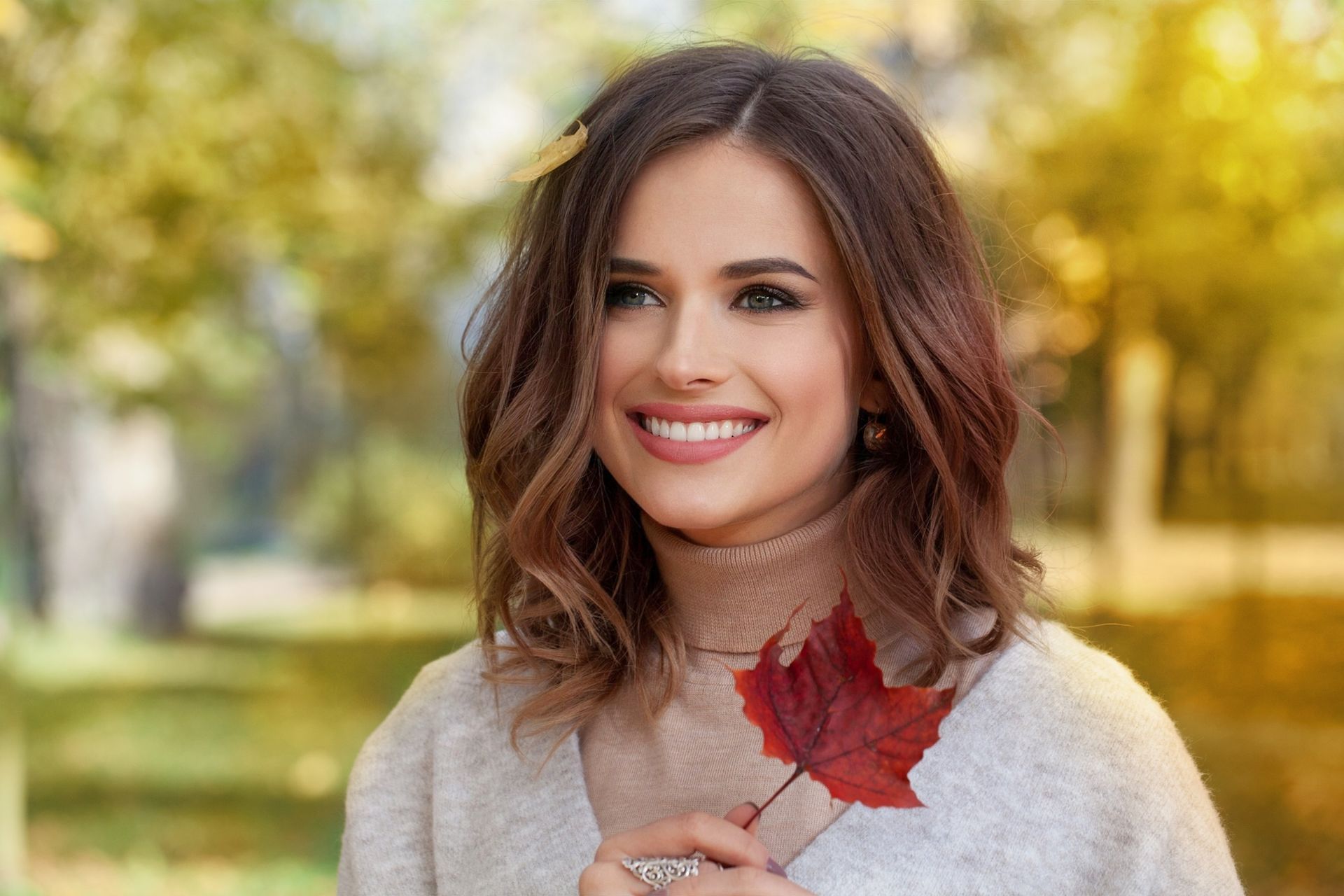 A woman with beautiful and healthy skin is smiling while holding a maple leaf in her hand.