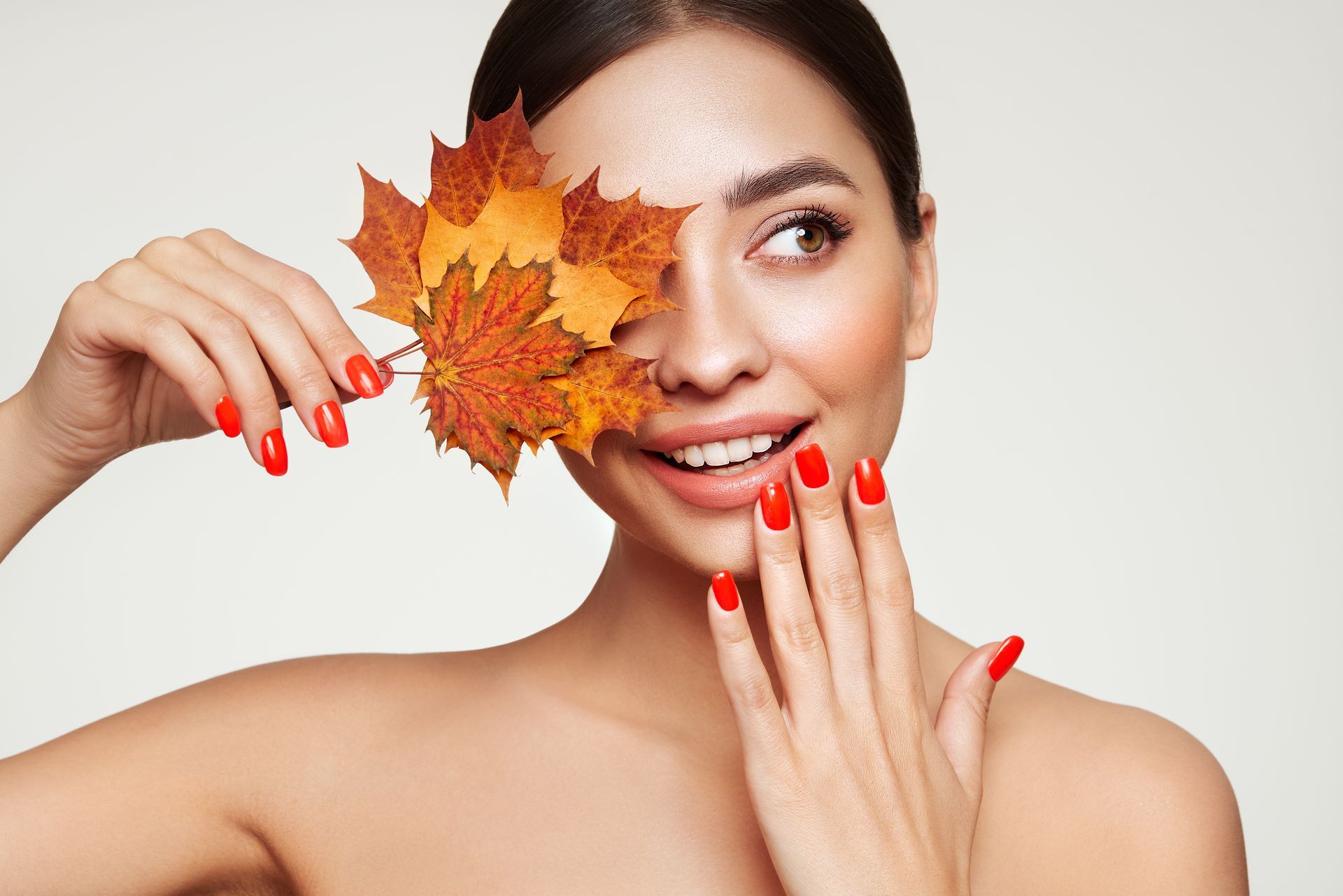 A woman with beautiful makeup is covering one eye and eyebrow with a maple leaf.