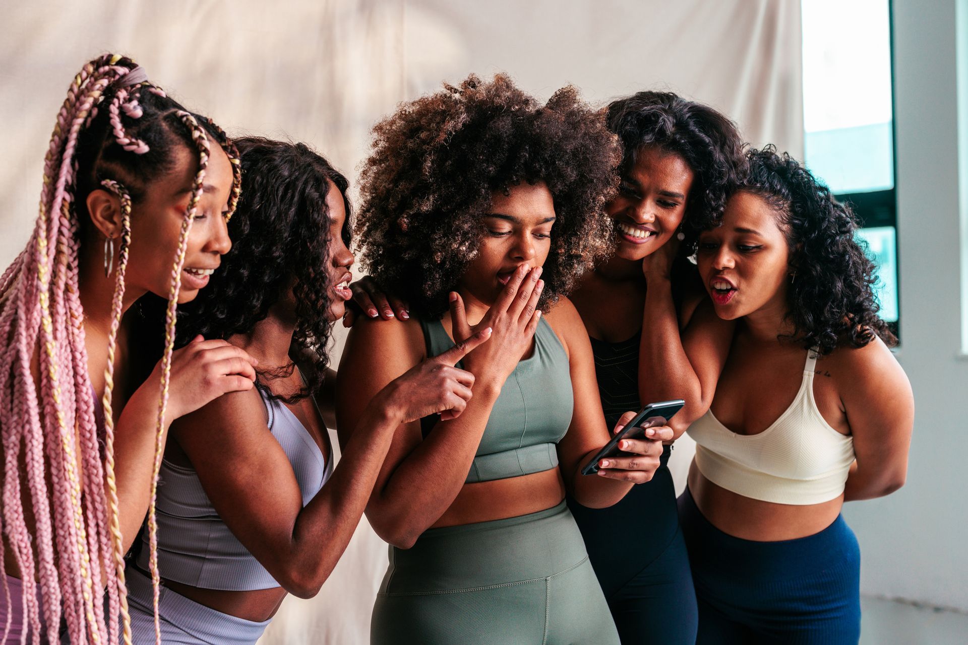 A group of women are standing next to each other looking at a cell phone.