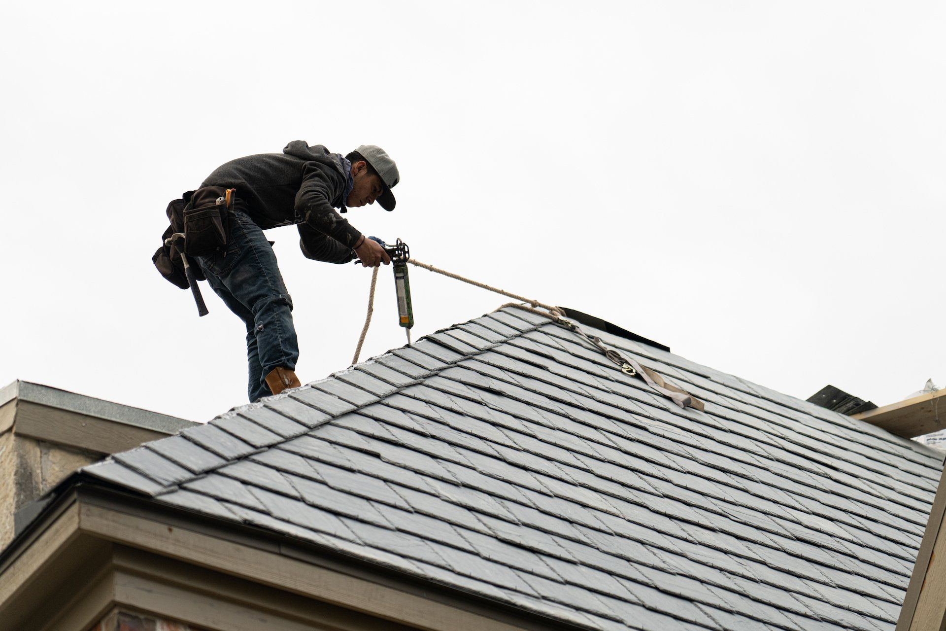 Roofer on a roof, securing something with a rope. Cloudy sky overhead.