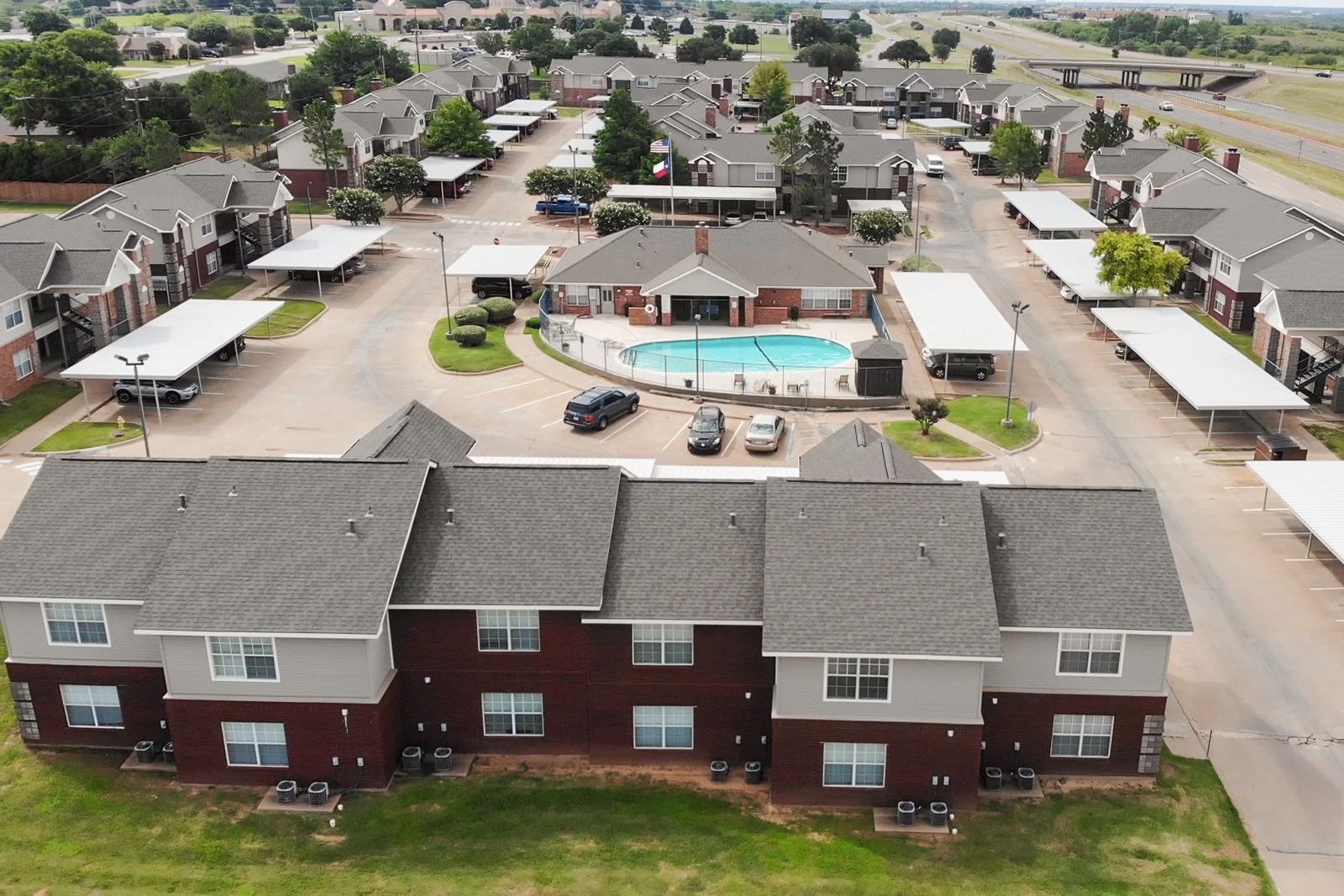 Aerial view of a multi-building apartment complex with a central swimming pool and covered parking areas.