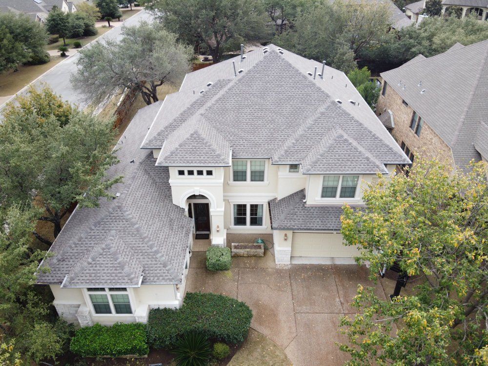 an aerial view of a large white house with a gray roof surrounded by trees .