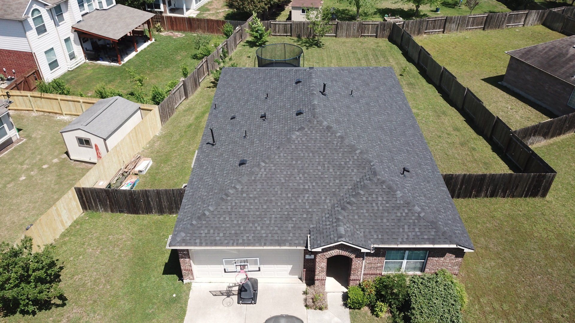 Aerial view of a house with a dark gray roof and yard surrounded by a wooden fence.