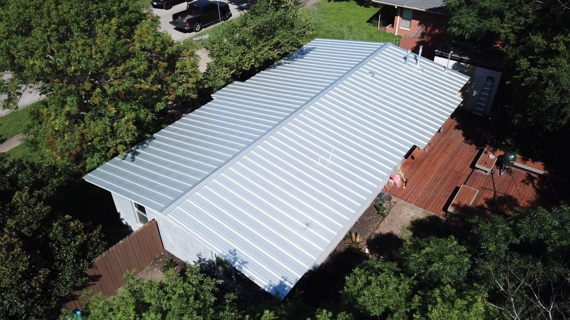 Aerial view of a house with a large white metal roof surrounded by dense green trees