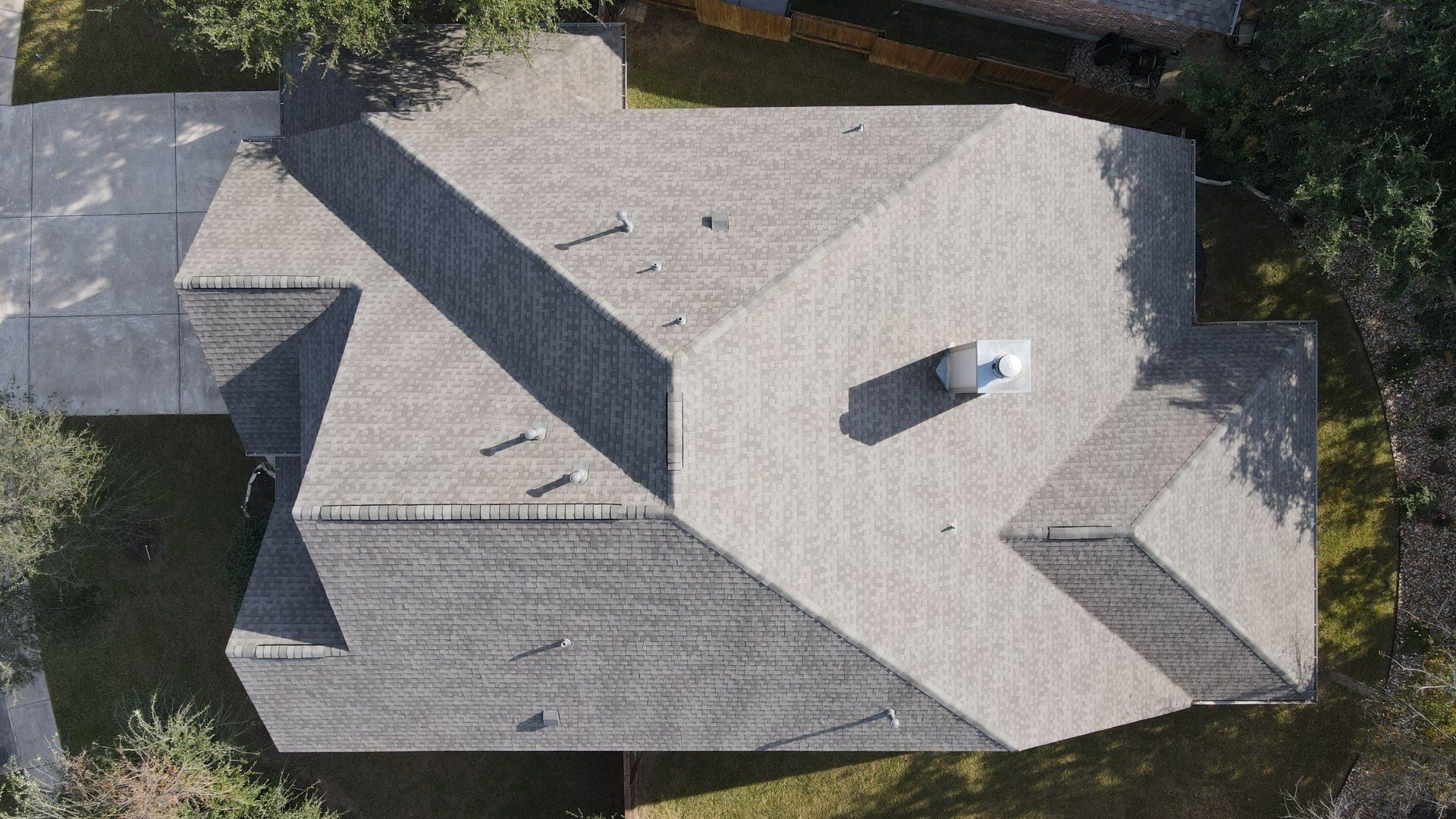 Overhead view of a house with a gray roof, chimney, and surrounding trees. A concrete driveway is on the left.